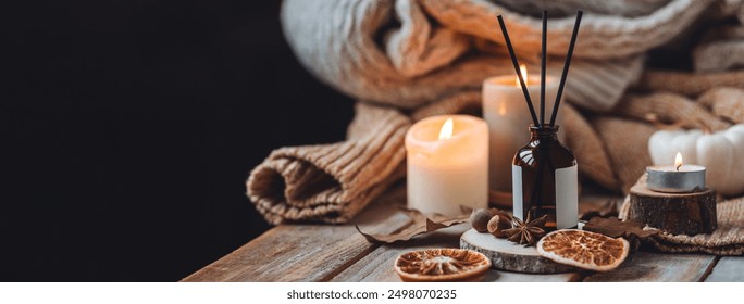 Home comfort, coziness, aromatherapy. Cozy interior with knitting, burning candles and aroma perfume diffuser in the living room. Fall scent, sweet pumpkin pie fragrance dry leaves, autumn mood banner - Powered by Shutterstock