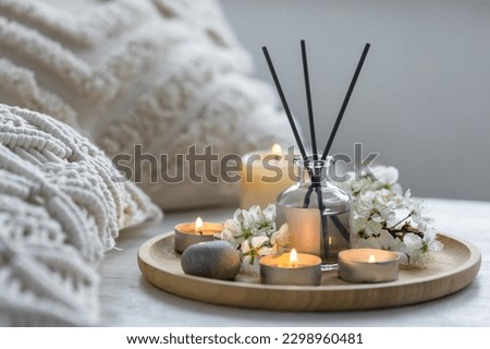 Home comfort, coziness, aromatherapy. Cozy interior with knitting, burning candles and aroma perfume diffuser in the living room. Fresh spring blossom fragrance, apple cherry flowers.