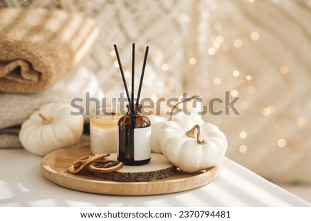 Home comfort, coziness, aromatherapy. Cozy fall interior with knitted wool warm sweater, burning candles and autumn aroma perfume diffuser in the bedroom. Pumpkin pie, cinnamon, anise