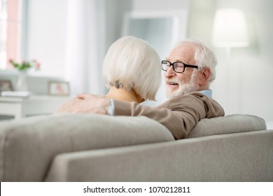 Home comfort. Happy elderly couple sitting on the sofa while smiling to each other
