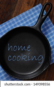 Home Cooking Concept With Text Added To Still Life Of Vintage Cast Iron Skillet On Rustic Background.  Ideal For Use As Menu Design Or Cookbook Cover.