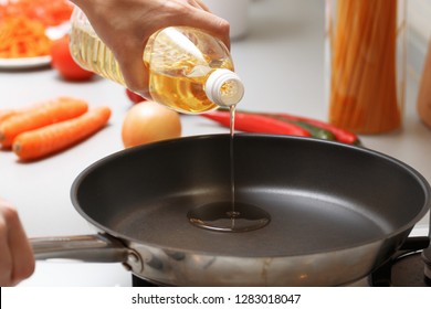 Home Cooking. A Woman Pouring Oil From A Bottle Into The Pan In The Kitchen, Near Fresh Vegetables And Pasta.