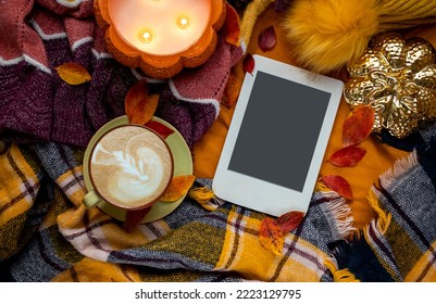 Home cozy composition with cup of coffee, warm checkered plaid, burning candle, e-book with copy space and autumn leaves. Cozy morning. Hygge home interior. - Powered by Shutterstock