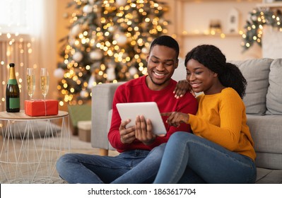 Home cozy in New Year and Christmas and video call to friends or family. Happy millennial african american lovers guy and lady talking on digital tablet in living room interior with tree with garlands - Powered by Shutterstock