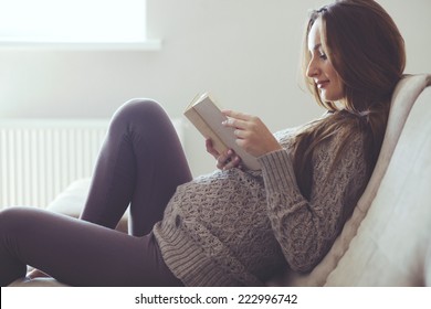 Home cozy portrait of pregnant woman resting at home and reading book on sofa - Powered by Shutterstock