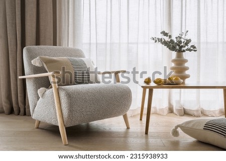 Home decor and furnishing concepts. Elegant armchair with cushions in bohemian style near wooden table with lemons and flowers in white geometric vase. Expensive design objects in apartment interior
