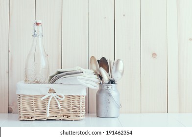 Home Decor: Glass Bottle And Wicker Basket And Vintage Cutlery On A Wooden Board Background, Cozy Kitchen Arrangement In Retro Style, Soft Pastel Colors.
