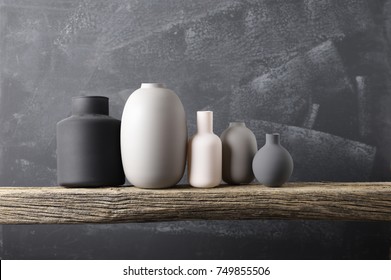 Home decor - various neutral colored vases on rough distressed wooden shelf against grey wall.