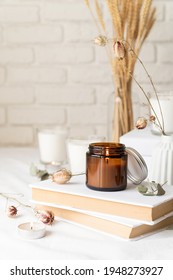 Home Decoration And Interior. Beautiful Burning Candles With Eucalyptus Leaves And Dry Flowers On Pile Of White Books