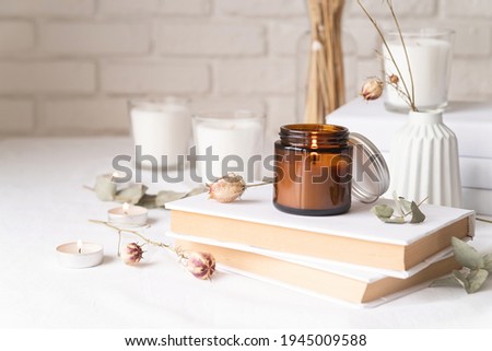Home decoration and interior. Beautiful burning candles with eucalyptus leaves and dry flowers on pile of white books