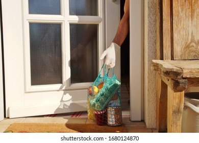 home delivering some groceries at quarantine time because of coronavirus infection COVID-19. man's hand is taking a shopping bag at he front door. Food delivery in net bag at door for self isolation - Shutterstock ID 1680124870