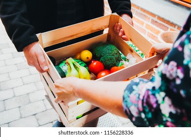 A Home Delivery From Man With Groceries At The Front Door Handling Over To Woman