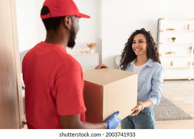 Home Delivery Service Concept. Portrait Of Smiling Young Woman Receiving Big Cardboard Box From African American Courier Guy In Protective Gloves Standing At Door, Delivering Order And Purchases