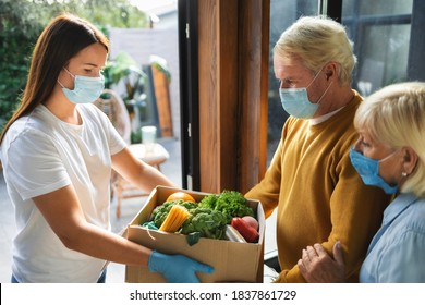 Home Delivery Service Young Woman Handing Fresh Food In Cardboard Box To Adult Couple. Donation Or Online Food Delivery. Virus And Quarantine Concept