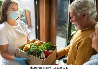 Home delivery service young woman handing fresh food in cardboard box to adult couple online - Powered by Shutterstock