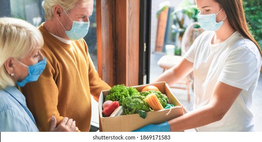 Home delivery service young woman handing fresh food in cardboard box to adult couple, virus and quarantine concept - Powered by Shutterstock