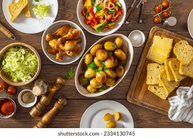 Home dinner table with set of various food from baked new potatoes, fried chicken legs and salads on wooden table top view