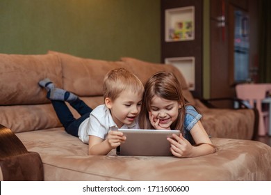 home distance learning at home. twins brother and sister are studying at home using a tablet. they are happy and laughing while lying on the couch