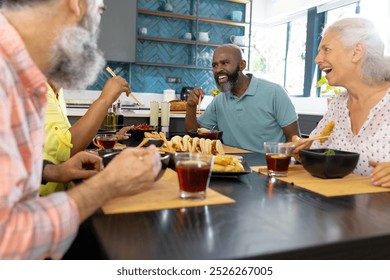 At home, Diverse group of senior friends enjoying meal and laughing together in kitchen. seniors, dining, laughter, togetherness, unaltered - Powered by Shutterstock