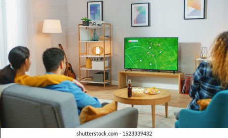 At Home Diverse Group of Sports Fans Watches Important Soccer Match on TV, They Cheer for the Team. Cozy Room with Snacks and Drinks on the Table. - Powered by Shutterstock