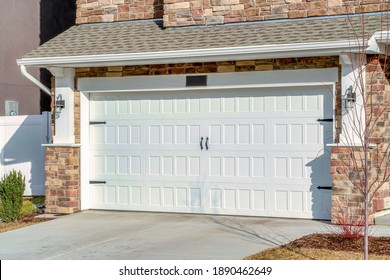 Home with driveway leading to hinged white garage door against stone brick wall