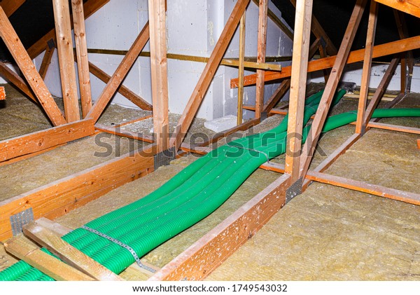 Home energy recovery ventilation, visible system of\
green flexible pipes for air transport, spread over the roof\
trusses with visible rock\
wool.