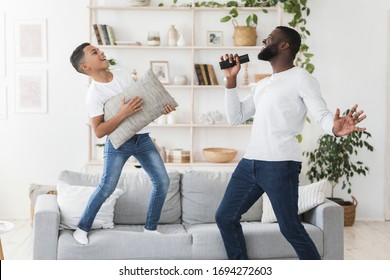 Home Entertainment. Happy african american father and little son having fun together in living room, playing and singing, boy using pillow as guitar - Powered by Shutterstock