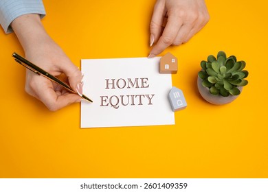 Home equity concept. Difference between the current market value of your home and the outstanding balance of any loans or mortgages secured by the property. A woman writes in notes. Real estate