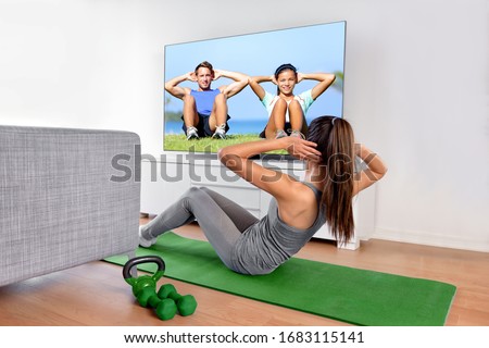 Home fitness concept. Woman doing strength training abs situps bodyweight floor exercises watching a dvd workout or web videos on a smart tv in the living room of a house or apartment.