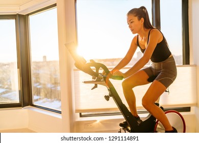 Home fitness workout woman training on smart stationary bike indoors watching screen connected online to live streaming subscription service for biking exercise. Young Asian woman athlete.