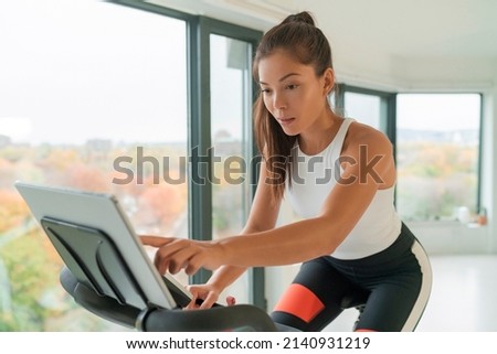 Home fitness workout woman training on smart stationary bike indoors watching screen connected online to live streaming subscription service for biking exercise. Young Asian woman athlete. Stock photo © 