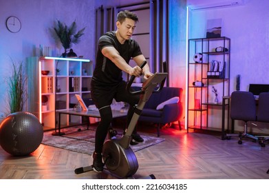 Home fitness workout, young asian man athlete training on smart stationary bike indoors watching on screen connected online to live streaming subscription service for biking exercise. - Powered by Shutterstock