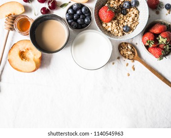 Home granola in a bowl, yogurt in a glass, coffee in a blue glass, fruits and berries on a table with a white tablecloth. Ingredients for healthy breakfast and coffee with milk. top view. - Shutterstock ID 1140545963
