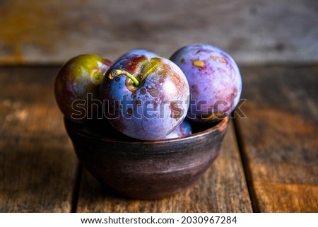 Home harvest fresh plums in a ceramic bowl on a wooden table.