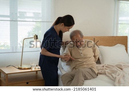 Home health care nurse caregiver take care senior elderly man at home she help support retirement oldman walking stick to bed
