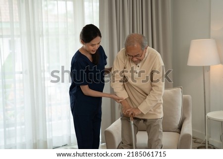 Home health care nurse caregiver take care senior elderly man at home she help support retirement oldman walking stick to bed
