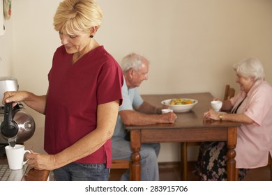 Home Help Sharing Cup Of Tea With Senior Couple In Kitchen