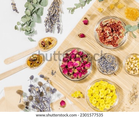 Home herbal apothecary concept. Sustainable flat lay with dry flowers and herbs, tea bags and wooden spoons on wooden napkin on white background. Healing tea from wild plants and flowers