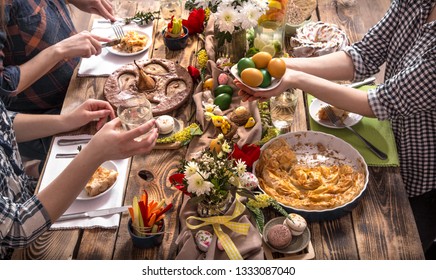 Home Holiday Friends Or Family At The Festive Easter Table With Easter Colored Eggs. The Concept Of The Celebration