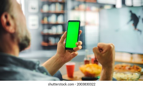 At Home Ice Hockey Fan Holds Green Screen Chroma Key Smartphone, Friends Watch Game On TV, Cheer For Favourtite Sports Team To Win Championship. Screen Shows Real Game. Over The Shoulder Close-up