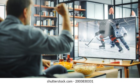 At Home Ice Hockey Fans Sitting On A Couch Watch Game On TV, Cheer When Favourtite Sports Team To Win The Championship. Screen Shows Professional Players During World Cup. Over The Shoulder