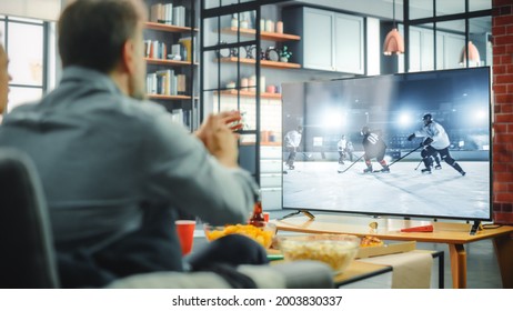 At Home Ice Hockey Fans Sitting On A Couch Watch Game On TV, Cheer When Favourtite Sports Team To Win The Championship. Screen Shows Professional Players During World Cup. Over The Shoulder