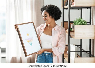 home improvement, decoration and people concept - happy smiling woman holding abstract watercolor picture in frame at shelf