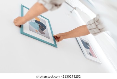 Home Improvement, Decoration And People Concept - Close Up Of Hands Hanging Picture In Frame On Wall