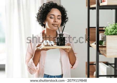 home improvement, decoration and people concept - happy smiling woman smelling aroma reed diffuser on board with cotton flower at shelf