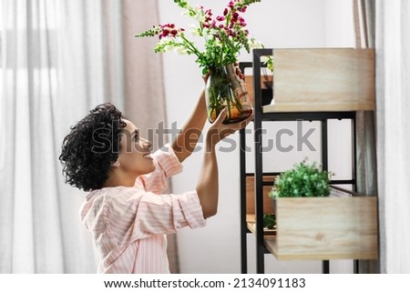 home improvement, decoration and people concept - happy smiling woman placing flowers to shelf