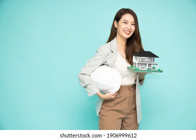 Home Inspector Asian Woman Or Engineer Holding A White Helmet And Single-family Home Or Detached House Model Isolated On Green Background