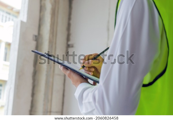 home inspector engineer in green reflective\
jacket checking review document and inspecting with clipboard at\
construction site building interior, construction, contractor and\
engineering concept