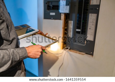 home Inspector in front of electric distribution board during inspection, selective focus and close up on man's hands as he holding notebook and pen