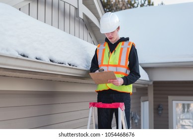 Home Inspector On A Ladder While Writing On A Clipboard During Winter. 